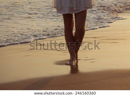 Girl walking along the ocean beach. View of legs and bare feet.