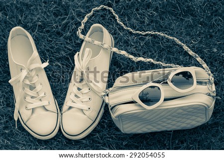 Sunglasses on a purse and sneakers with grass as a background. Retro style effect. Summer fashion look concept