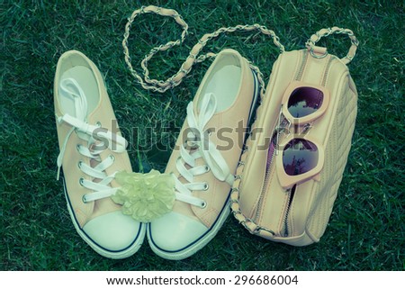 Sunglasses and purse, sneakers with white rose  with green grass as a background. Summer fashion look concept. Toned effect