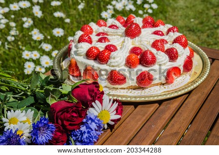 Bouquet of summer flowers at a table with homemade strawberry cake in a garden