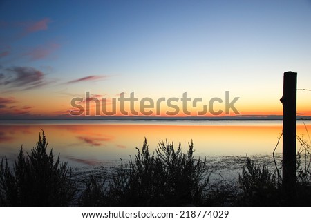 Silhouette of a post at sunset with colored sky at a calm bay