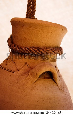 Neck, handle and top of a brown pottery jar hanging from a brown rope.