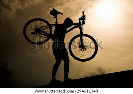 Man with mountain bicycle lifted above him  in the evening