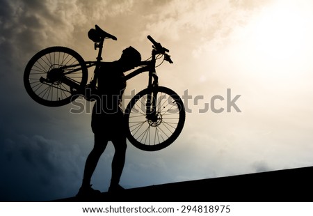 Silhouette of a man with mountain bicycle lifted above him.