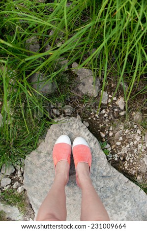 Overhead photo of feet on a background of big stone and grass. Women feets view from above. Exploring, travelling, tourism, leisure.