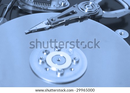 Closeup of the platters and read/write head of a computer hard drive in blue light