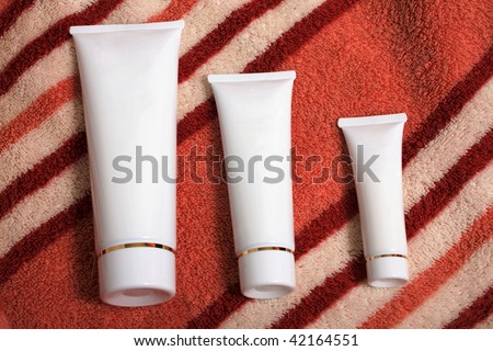 Three white tubes with cosmetic cream on a towel