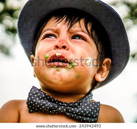 Close up outside shot of crying latino baby with cake frosting on his face