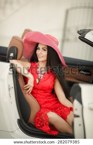 Fashionable young woman in car smiling girl in hat summer portrait beautiful female in red dress outdoors, sexy fashion woman model in luxury car, soft focus, series