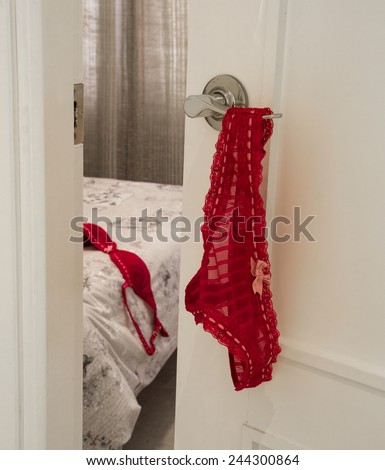 Invitation to the bedroom. Red panties on a door knob with bra in a background on the bed. Love, seduction, passion. Valentines mood.