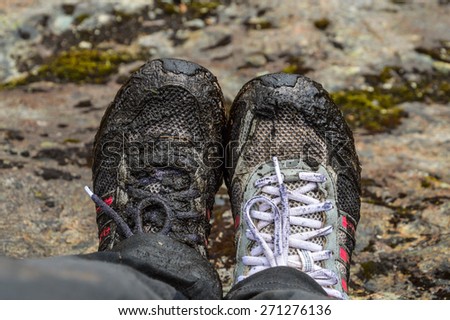 Dirty sport shoes after walking on a muddy trails of Las Cajas National park in Ecuador. Close up on a shoes and piece of leg. One shoe is completely black, covered with mire (dirt).