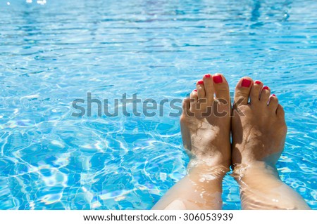 Feet in the swimming pool. Relax, vacation, summer. Red nails, suntanned skin, turquoise water. Sunlight dancing in the water. Summer holidays, relaxation, enjoyment, tanning. Floating on the surface