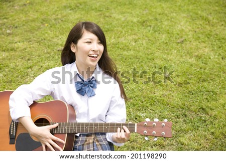 The high school girl playing the guitar while sitting on the hill