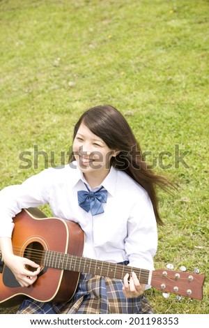 The high school girl playing the guitar while sitting on the grass