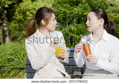 Two women who drink drink in the park bench