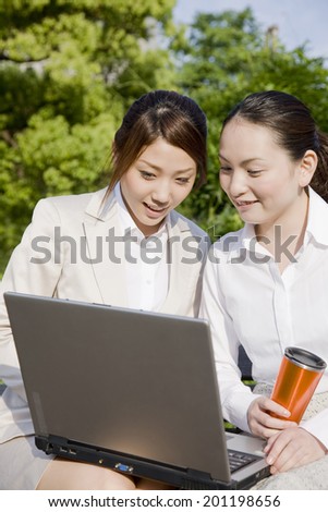 Two women looking at a laptop on a bench in the park