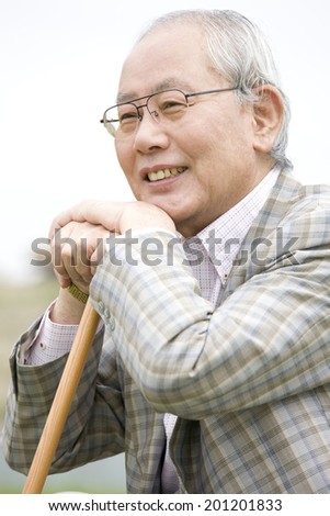 The laughing old man while supporting his jaw on a cane and sitting on the bank