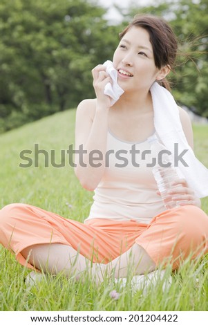 The woman wiping the sweat with a towel while sitting on the hill
