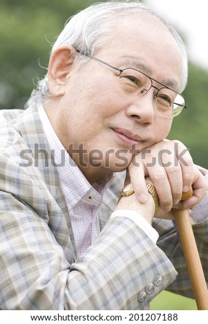 The laughing old man while supporting his jaw on a cane and sitting on the bank