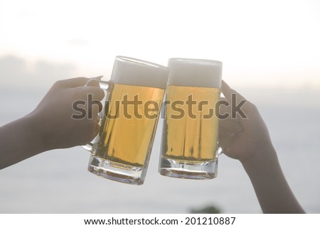 The hands of two women making a toast with beers