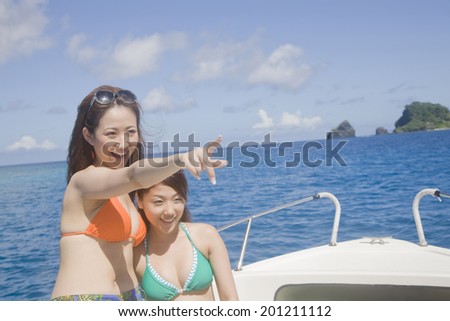 Two women with a swimming suit pointing at the other side of the sea on the yacht