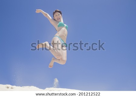 The woman with a swimming suit jumping on the beach