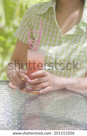 The hand of a woman chatting with friends over a cup of juice at a cafe surrounded by fresh green