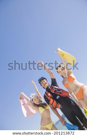 Two swimsuit women taking a commemorative photograph with a webbed foot under the blue sky and the man with a diving suit