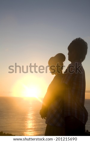 The silhouette of the man hugging from the behind of the woman at dusk