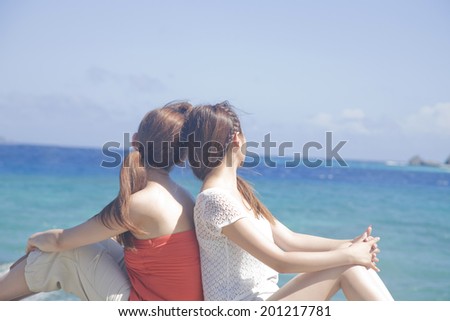 Two women sitting on the seaside with back-to-back