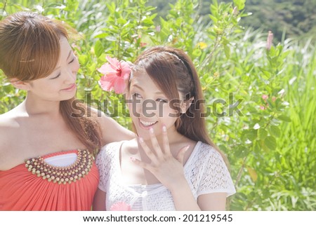 The woman trying to stick hibiscus flower on the head of the girl friend