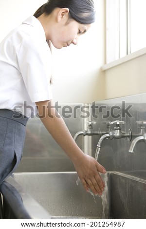 A middle school girl washing her hands under a faucet