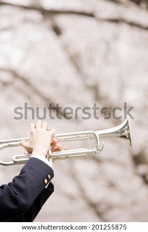 The hands of a middle school girl playing a trumpet under cherry blossoms