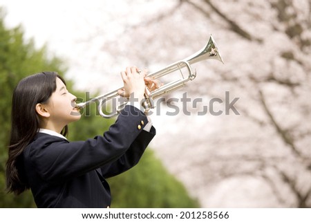 A middle school girl playing a trumpet under cherry blossoms