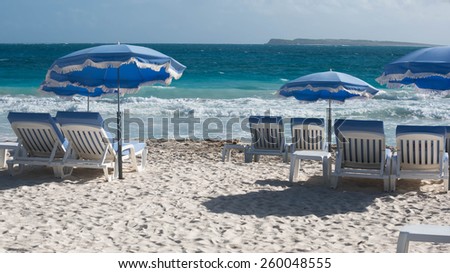 Blue umbrellas above white beach loungers on the white sand beach of Saint Martin