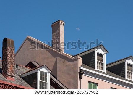 Early moon makes an appearance above chimney and roofs of typical suburban town.