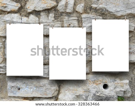 Three hanged paper sheets with clothes pins on ancient stone rock wall