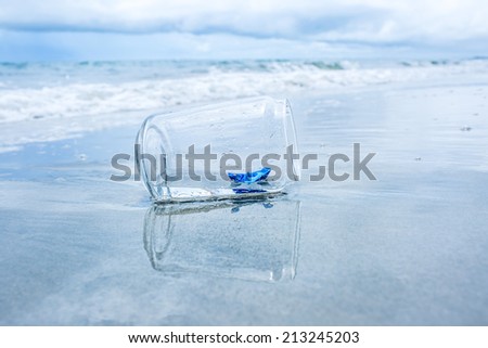 Blue paper boat in bottle on the beach.