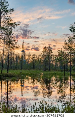 Siberian swamps under sunset skies with land oil drilling rig reflecting in water near Kogalym, Russia (West Siberia)