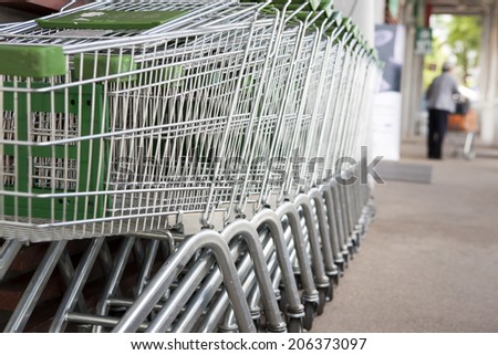 Many empty shopping carts in a row with old shopping female in background