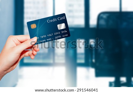 female  hand holding credit card against business office background