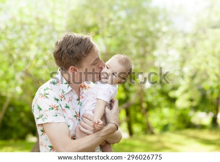 Father kissing his cute baby  outdoors in spring park against natural green background. family shot