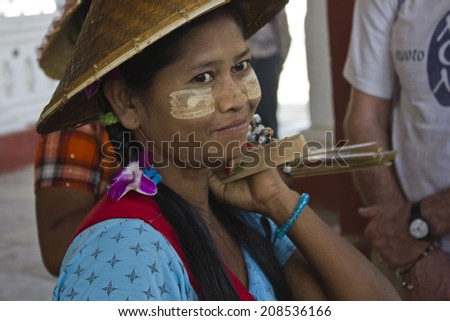 Mingun, February 27, 2014: Burmese girl with a fan. This girl sells fans outside the temple. In the face she has the traditional saffron cream to protect to the sun