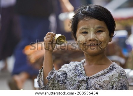 Yangon, Myanmar, February 27, 2014: Young Bells seller. A young unidentified girl selling bells in the street. In the face she has the typical Sandal-Saffron cream to protect the skin from the sun