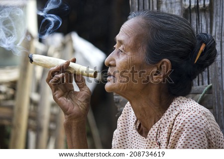 Bagan, Myanmar, March 2, 2014: Asiatic old woman smoking a big handmade cigar. Image taken in a little village , where a woman does cigars by herself and smoke them proudly in the middle of the street