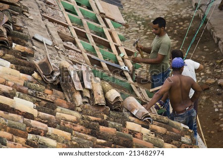 Trinidad, Cuba, August 18, 2012: construction workers standing on a roof covering it with wood and tiles tiles