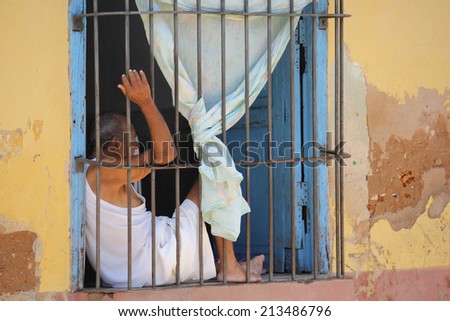 Trinidad, August 18, 2012. Life in trinidad, Cuba. Men behind its window. Daily Life in Trinidad, Cuba. Men inside its house's window.  The sbars make it seemd like a prison.