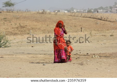 PUSHKAR, INDIA - NOV 28: A poor Indian Mother, orange dressed, with her son, standing on the sand in Pushkar on November 28 2012
