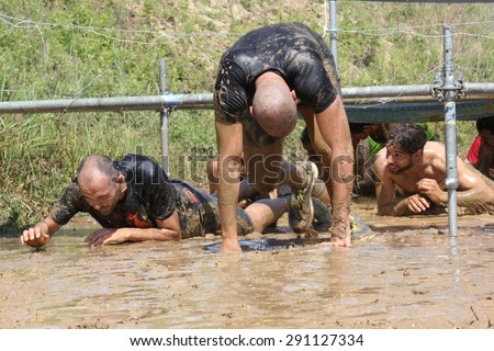 SIGNA, ITALY - MAY 9 2015: People passing  under the wires during the Inferno Run Mud Race competition near Florence, splashing in the mud