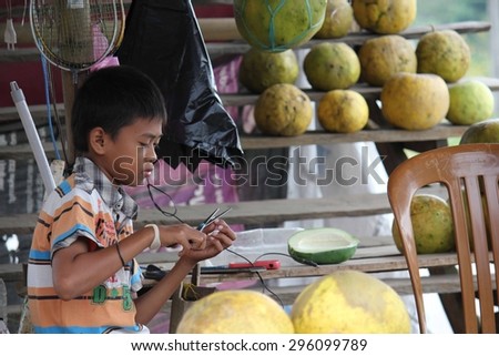 SULAWESI, INDONESIA - JULY 2 2012: Young Indonesian boy at work in a fruit stand on the street in the Sulawesi region of Indonesia